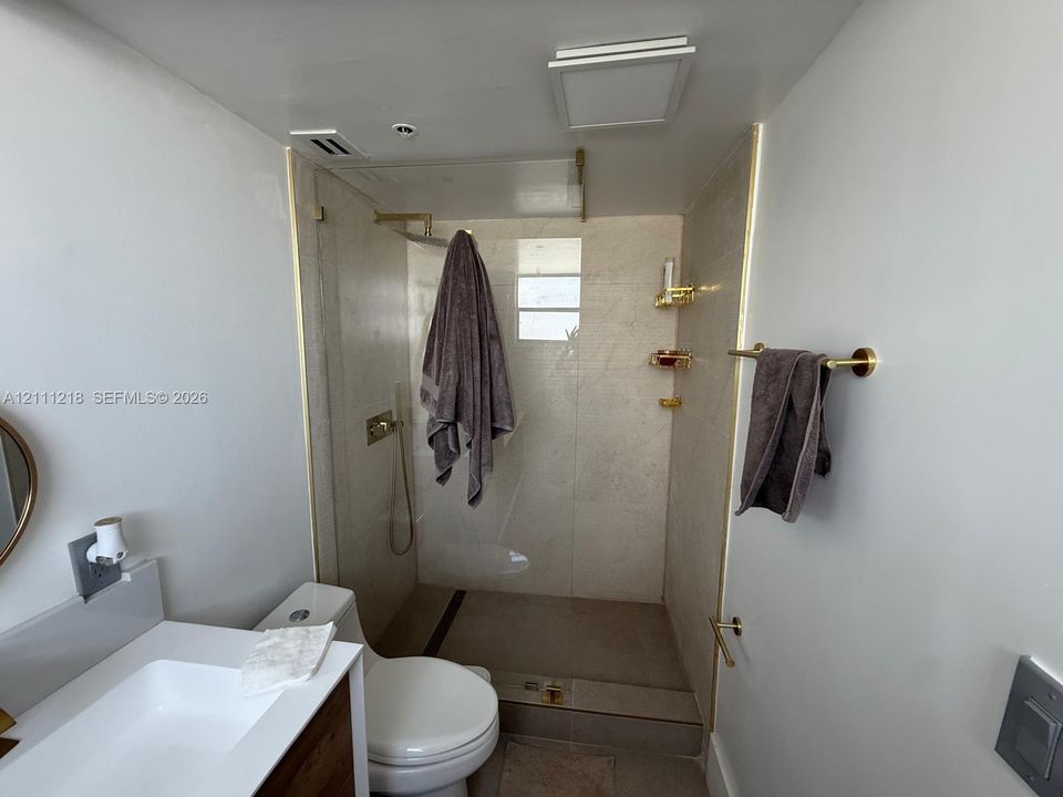 Walk-in shower featuring a frameless glass enclosure, gold-toned hardware, floor-to-ceiling stone-tiled walls, and a recessed stone shower floor