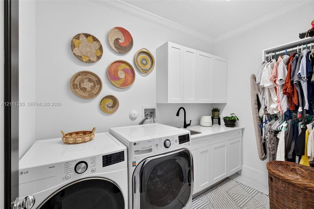 Laundry room featuring shaker-style upper and lower cabinetry, white quartz countertop, undermount sink with a matte black faucet, and patterned tile flooring