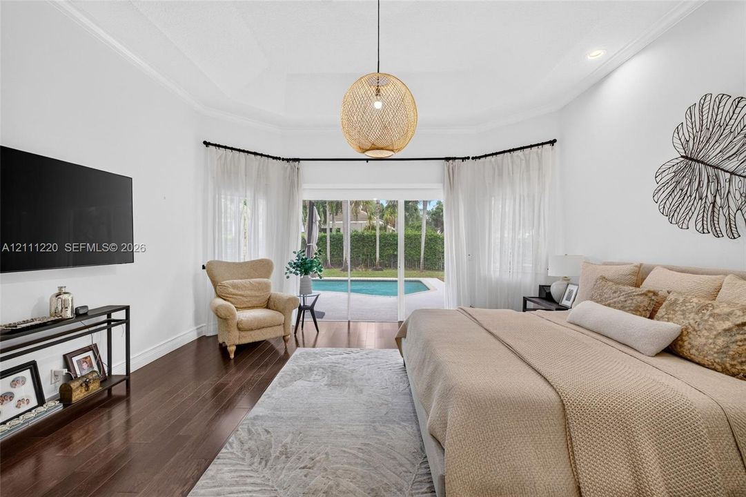 Tray ceiling, wood-finish flooring, and glass sliding doors providing exterior exposure to a swimming pool