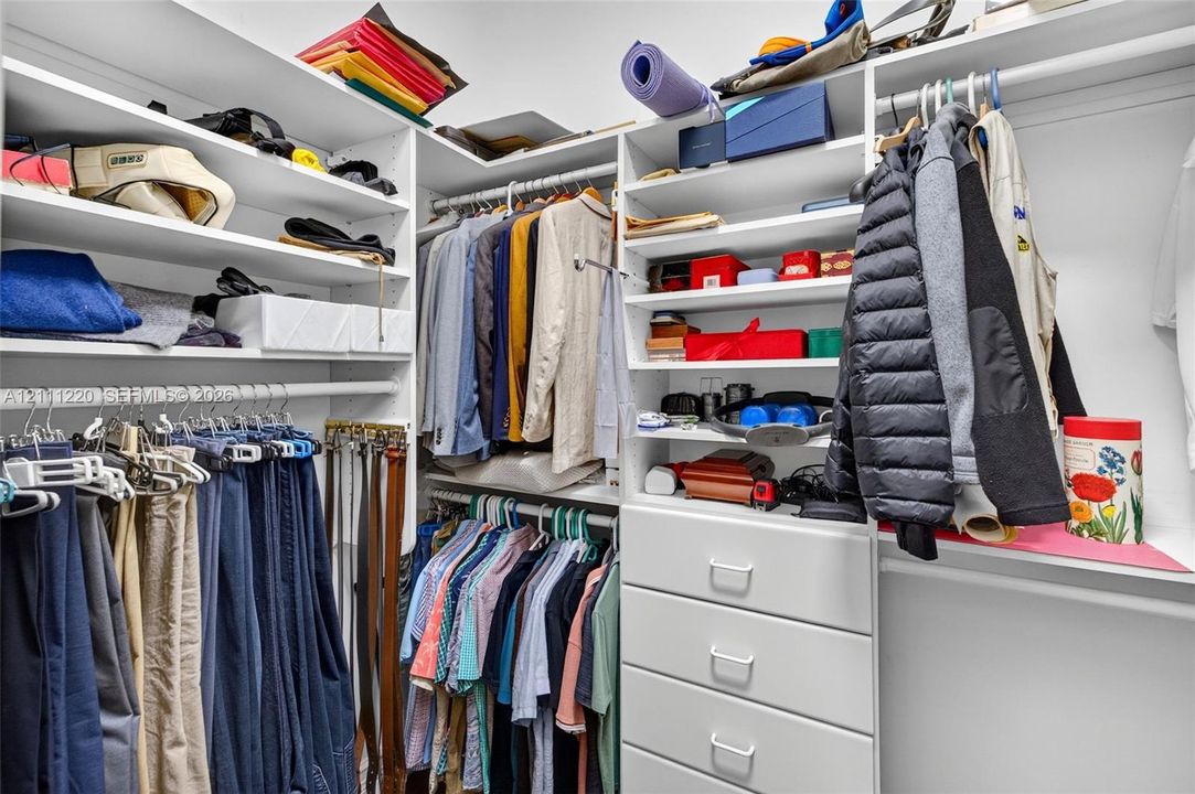 Walk-in closet featuring white built-in shelving, multi-level clothing rods, and a stack of four integrated storage drawers
