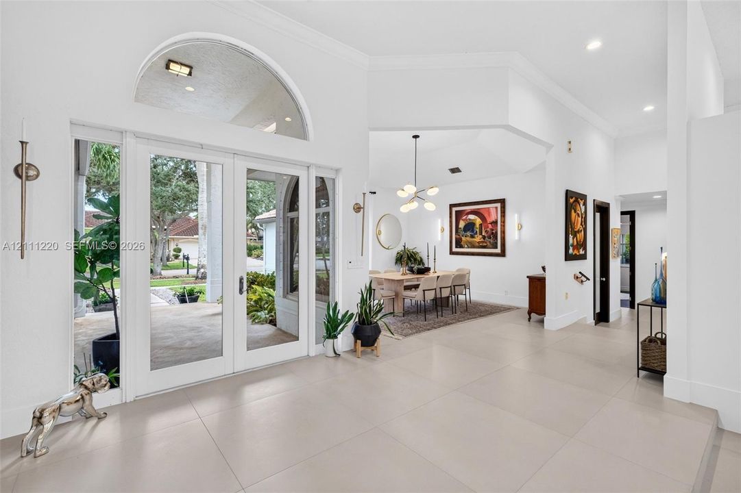 Foyer featuring large-format tile flooring, high ceilings, double glass entry doors with a decorative arch transom window, and crown molding