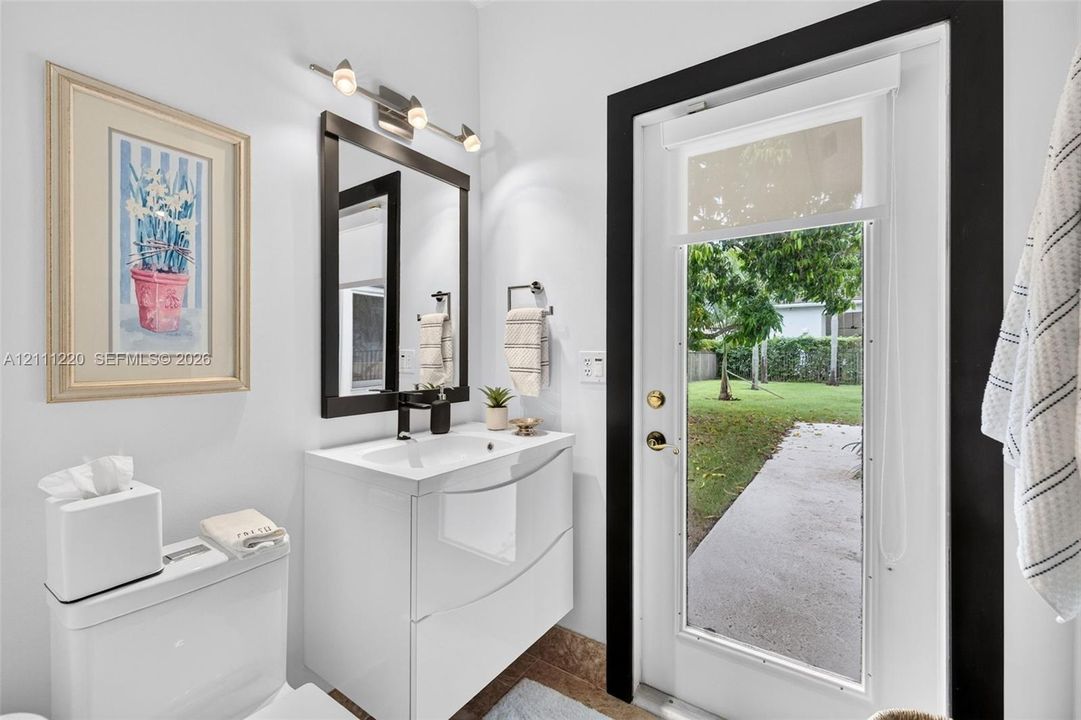 Modern floating vanity with a vessel sink, dark-framed vanity mirror, multi-bulb wall-mounted lighting, and an exterior glass door leading to a concrete walkway