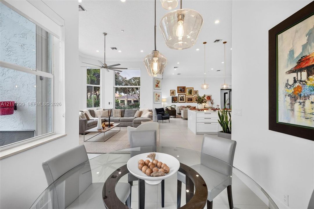 Open-concept interior featuring large-format tile flooring, recessed lighting, expansive windows, and tiered glass pendant fixtures over the dining area