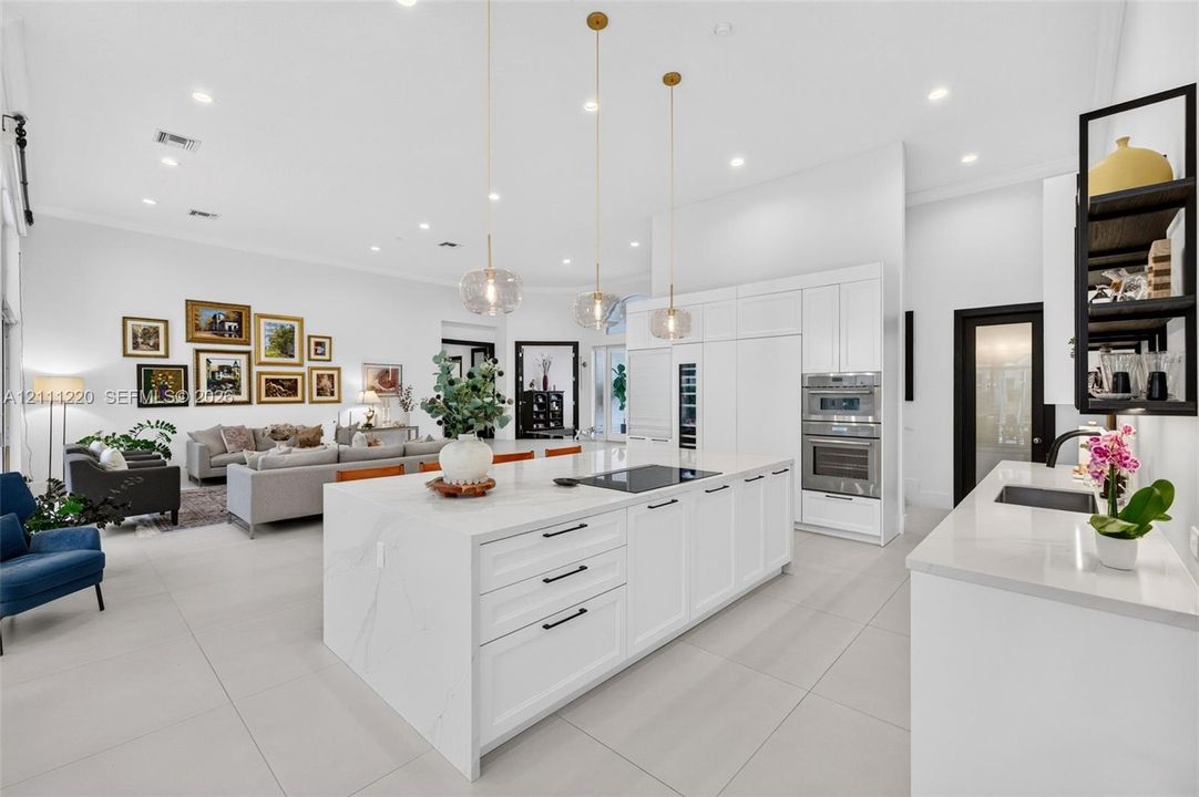 Kitchen featuring a large central island with quartz surfacing, white shaker-style cabinetry, stainless steel double wall ovens, three glass pendant light fixtures, and neutral oversized tile flooring
