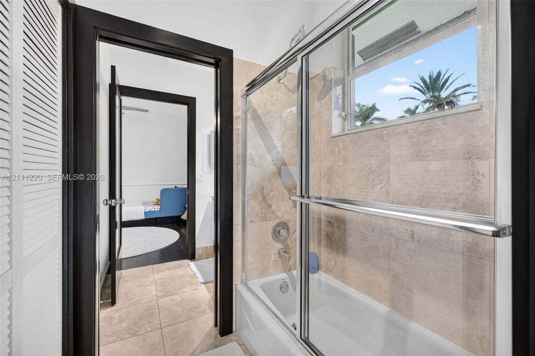 Full bathroom featuring a tub-shower combination with a sliding glass enclosure, large-format stone-finish wall and floor tiling, and dark-finished door trim