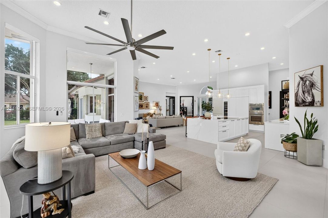Open-concept living area featuring high ceilings, recessed lighting, large-format tile flooring, a chef's kitchen with a waterfall island, and a multi-blade ceiling fan