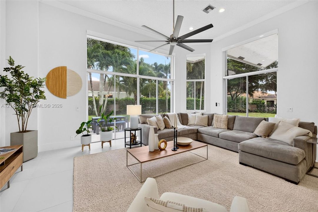 Expansive living area featuring vaulted ceilings, floor-to-ceiling windows, polished neutral flooring, and a multi-blade ceiling fan