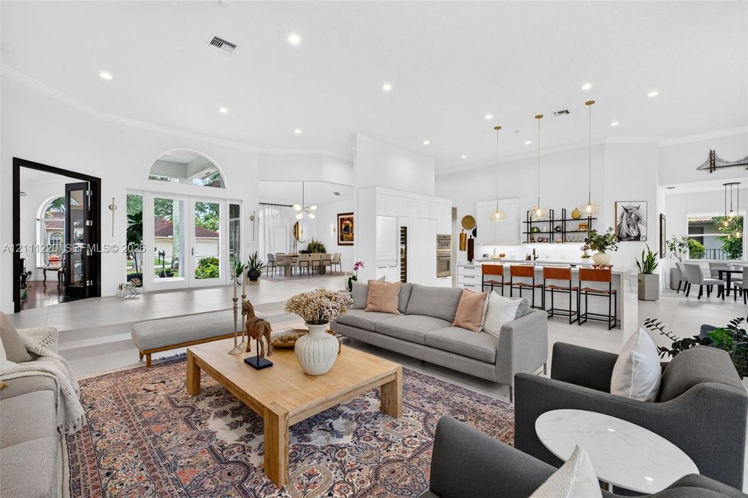 Open-concept interior featuring large-format tile flooring, recessed lighting, arched window accents, double glass-paned doors, and a kitchen island with pendant lighting