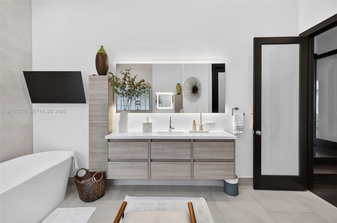 Floating wood-finish vanity with an integrated countertop, rectangular undermount sink, backlit rectangular mirror, and a freestanding soaking tub