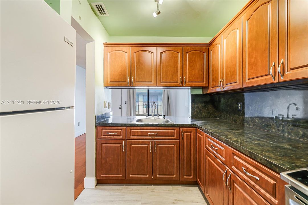 Kitchen featuring wood cabinetry, stone-finish countertops, stainless steel sink, and track lighting