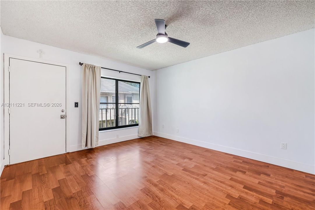 Room featuring wood-finish flooring, a matte black three-blade ceiling fan with integrated light, and a window with black framing