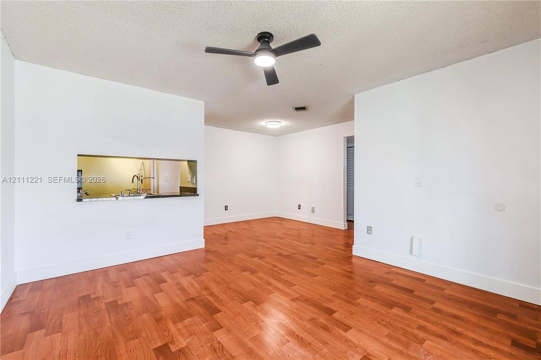 Interior space featuring wood-finish flooring, a wall cut-out opening, and a ceiling fan with integrated lighting