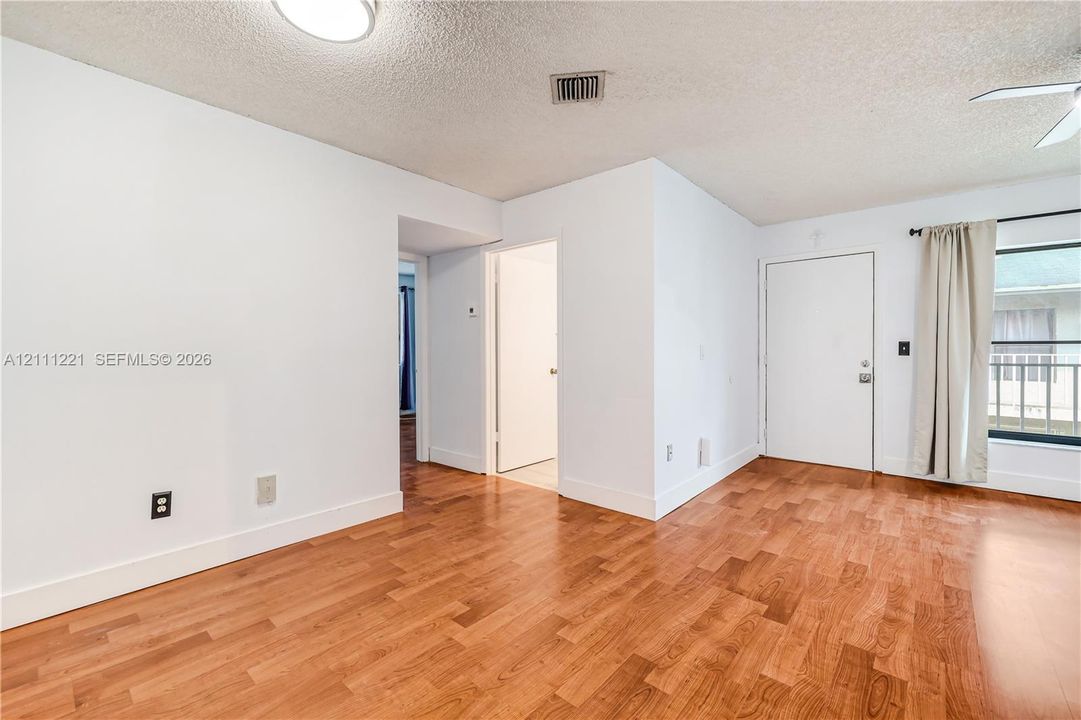 Interior space featuring wood-finish flooring, white walls, a flush-mount ceiling light, and a window with horizontal blinds