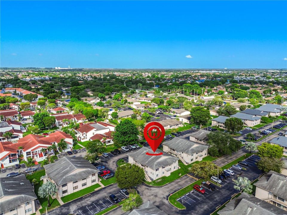 Aerial view of multi-unit residential building featuring a pitched shingle roof, exterior staircases, designated surface parking, and landscaped grounds