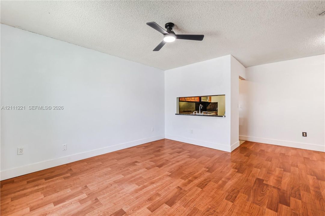 Interior space featuring wood-finish flooring, a matte black three-blade ceiling fan with integrated light, and a pass-through window to the kitchen area