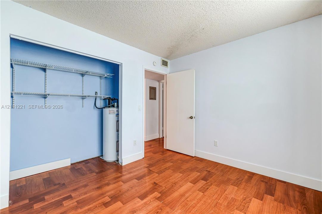 Room featuring wood-finish flooring, an open-concept closet with built-in metal shelving, and a cylindrical water heater