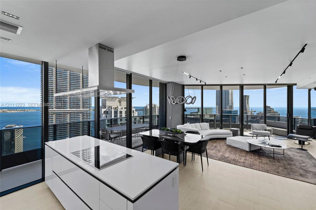 Open-concept kitchen featuring a white center island with a built-in cooktop, stainless steel range hood, floor-to-ceiling windows, light-toned flooring, and modern track lighting