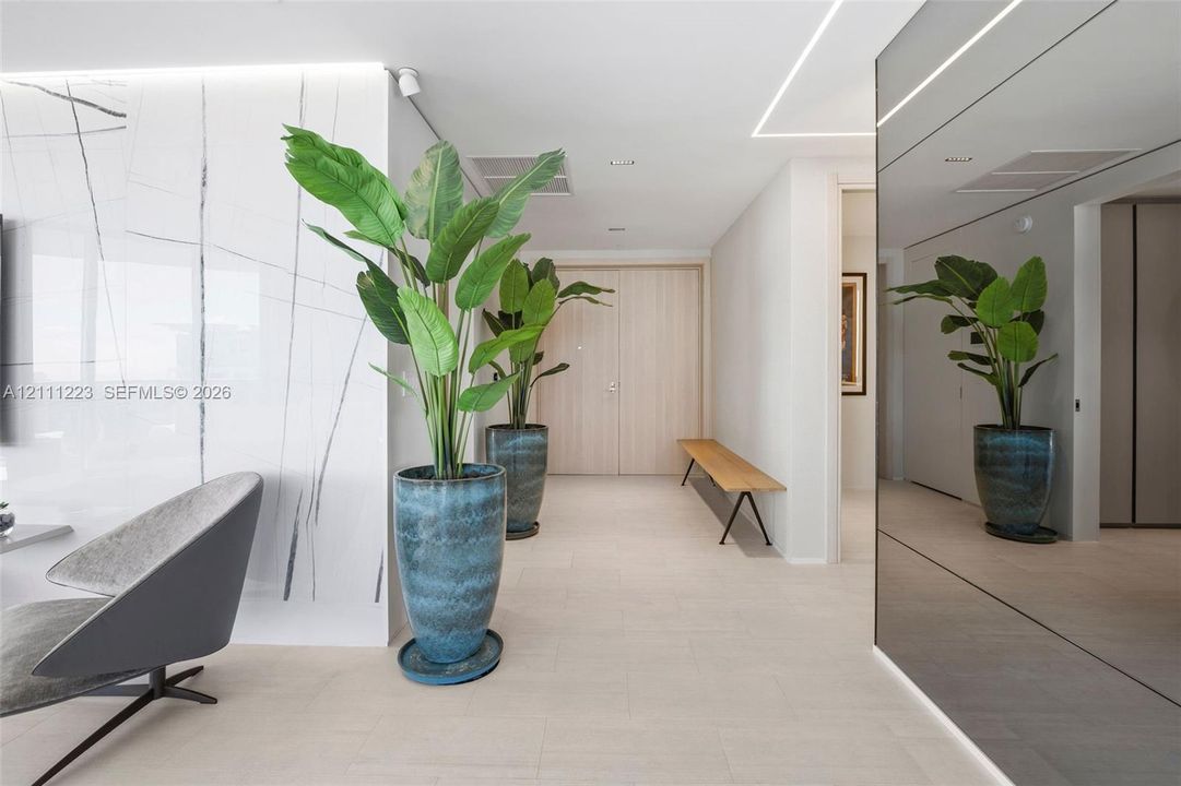 Large-format stone-style wall cladding with neutral veining, high-gloss mirrored wall paneling, linear recessed ceiling lighting, and smooth-finish flooring