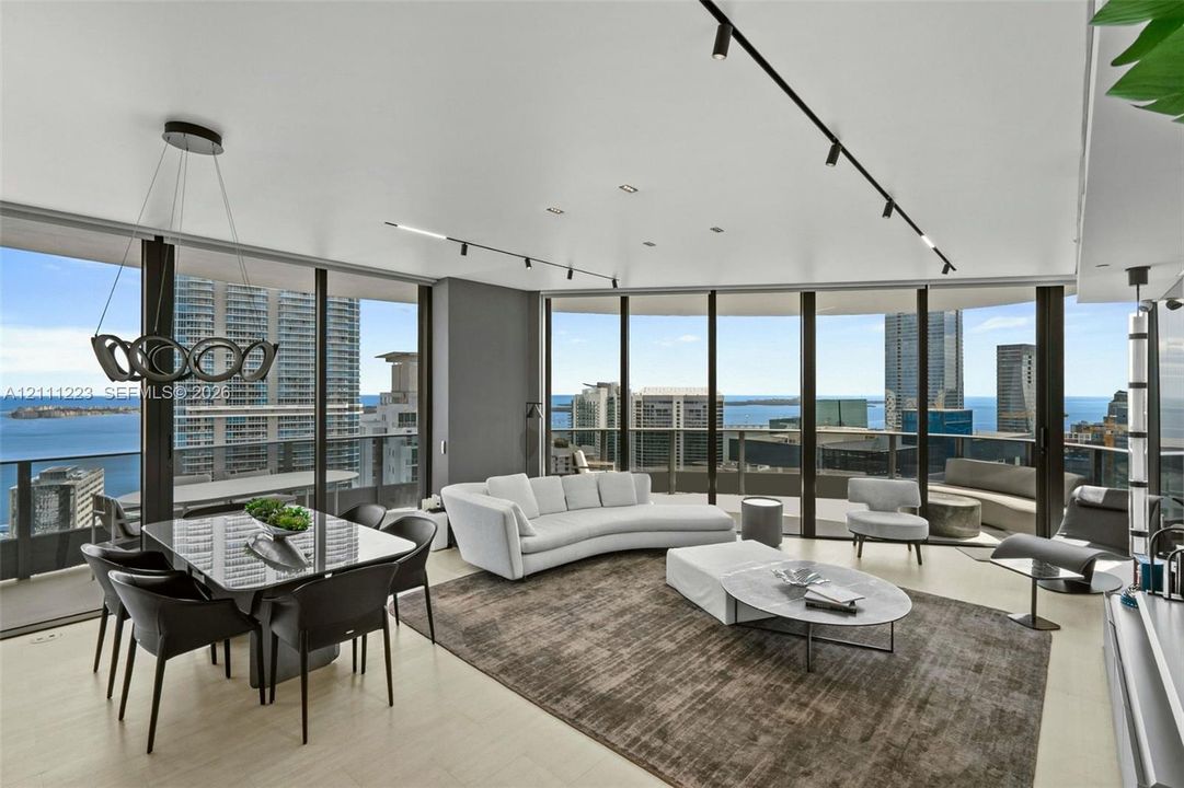 Open-concept interior featuring floor-to-ceiling glass windows, recessed track lighting, a geometric chandelier, and light-toned flooring