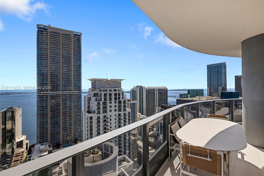 Curved private balcony with glass railing, concrete overhead covering, and panoramic urban and water scenery