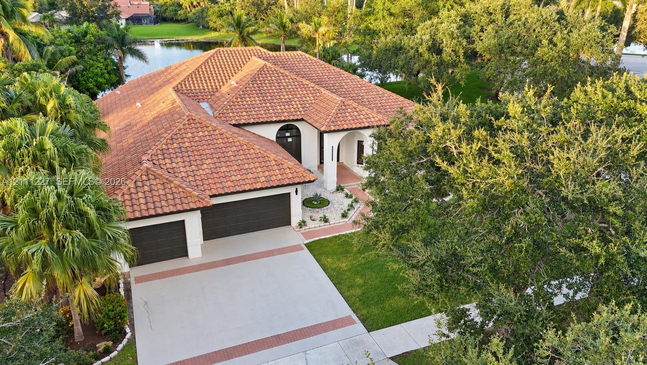 Mediterranean-style residence featuring a multi-pitched clay tile roof, stucco exterior, two-car garage, concrete driveway with decorative brick inlay, and waterfront location