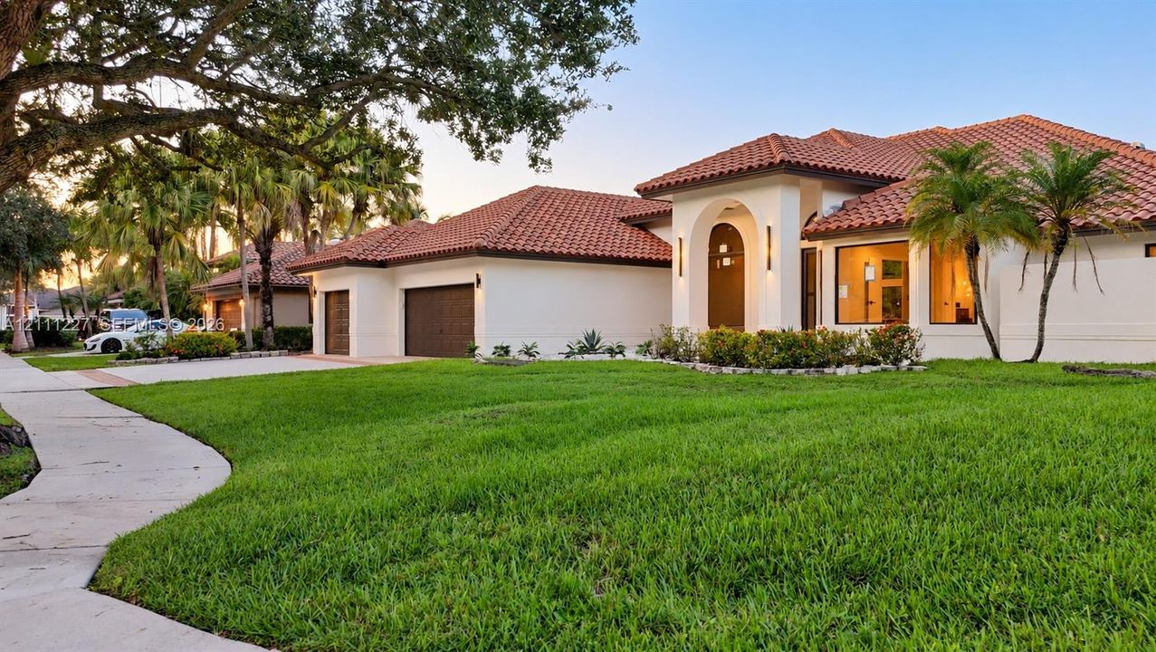 Stucco exterior featuring a terracotta tile roof, arched entryway, multi-car garage, and manicured landscaping