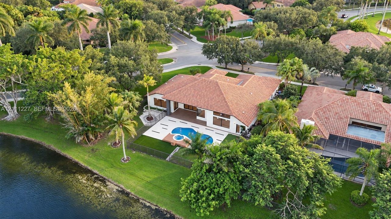 Aerial perspective of a single-story residence featuring a tile roof, a rear patio with an inset swimming pool and spa, and expansive lawn space with mature landscaping
