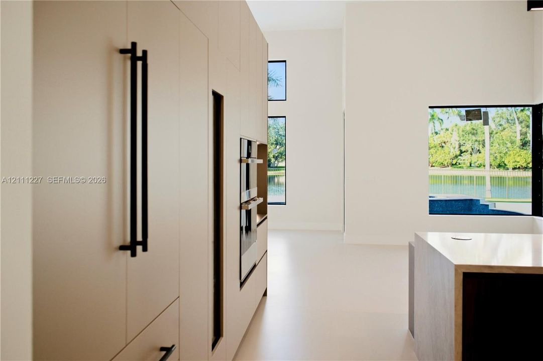 Full-height, flat-panel cabinetry featuring matte black hardware, integrated double wall ovens, expansive floor-to-ceiling windows, and a waterfall-edge stone island