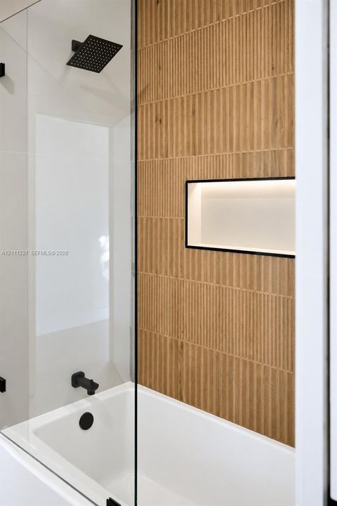 Walk-in shower enclosure featuring floor-to-ceiling vertically textured tile, a built-in recessed niche, a matte black rainfall shower head, and matching black hardware