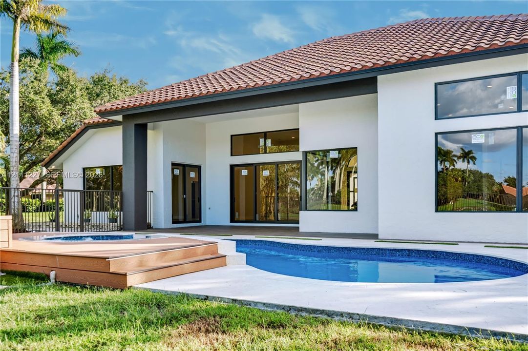 Rear exterior featuring a stucco facade, clay tile roof, swimming pool with tiled finish, raised composite decking, and expansive glass window panels