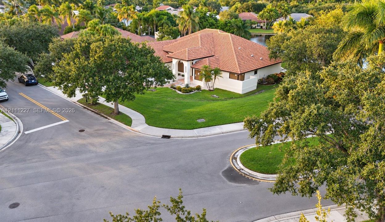Corner lot property featuring a multi-gabled terracotta tile roof, stucco exterior, expansive lawn, and mature landscaping