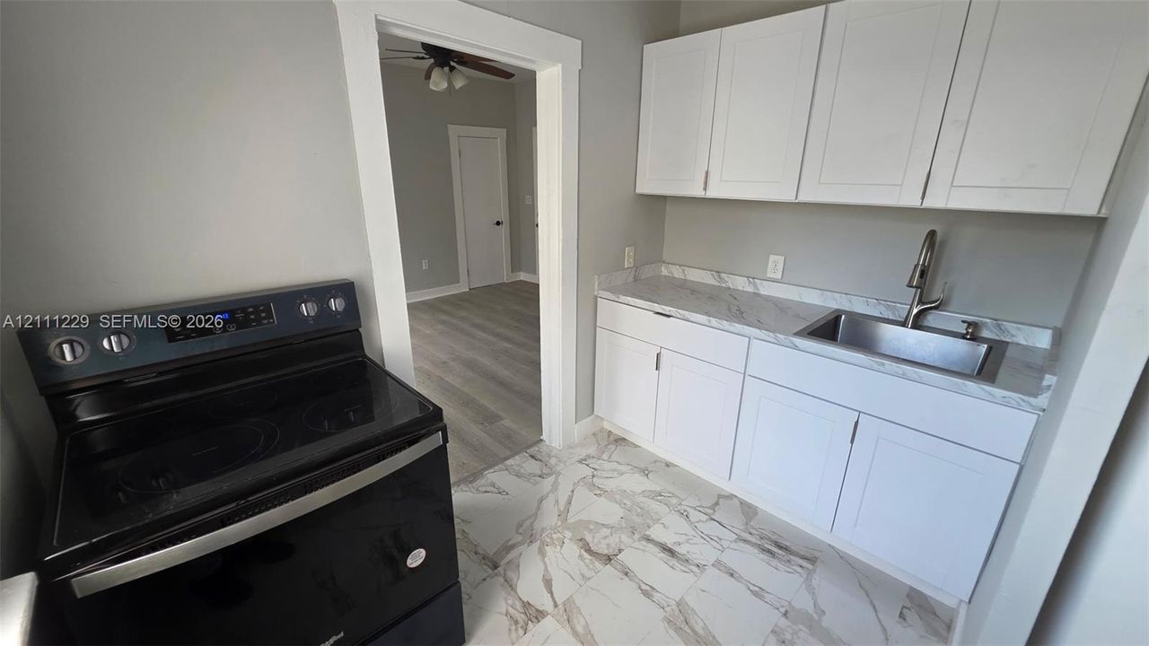 Kitchen featuring white shaker-style cabinetry, stone-patterned laminate countertops, stainless steel undermount sink with gooseneck faucet, black electric range, and large-format porcelain tile flooring
