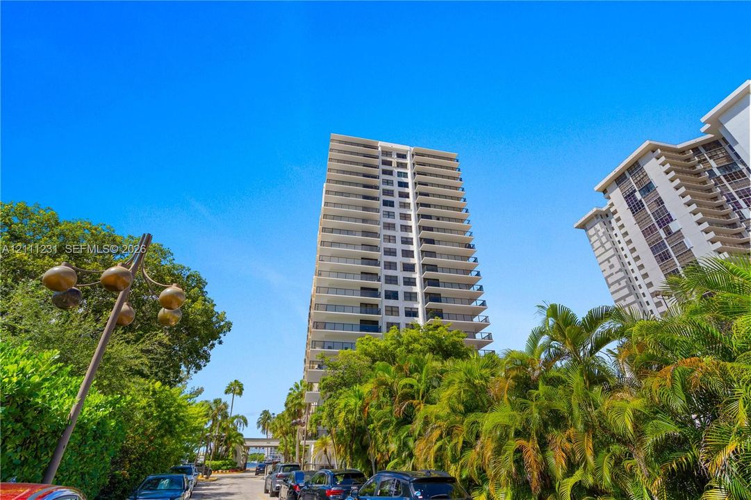 High-rise residential building featuring private balconies, expansive windows, and mature tropical landscaping