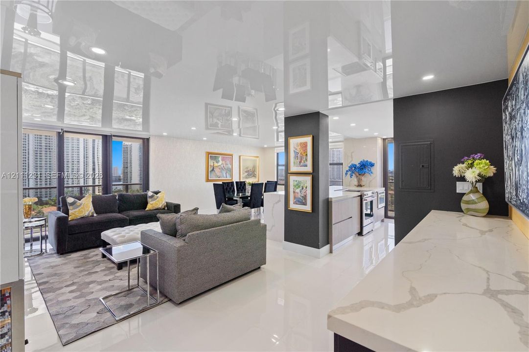 High-gloss reflective ceiling, stone countertop with waterfall edge, recessed lighting, floor-to-ceiling windows, and polished porcelain flooring