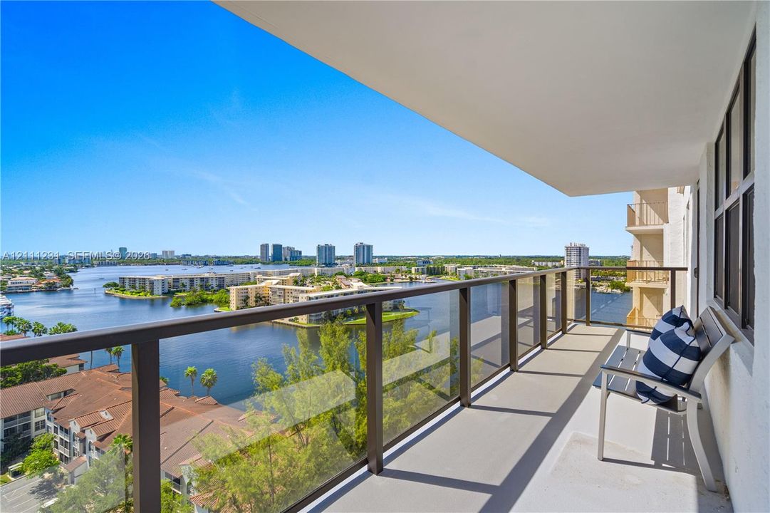 Covered balcony featuring glass pane railings, solid surface flooring, and water frontage