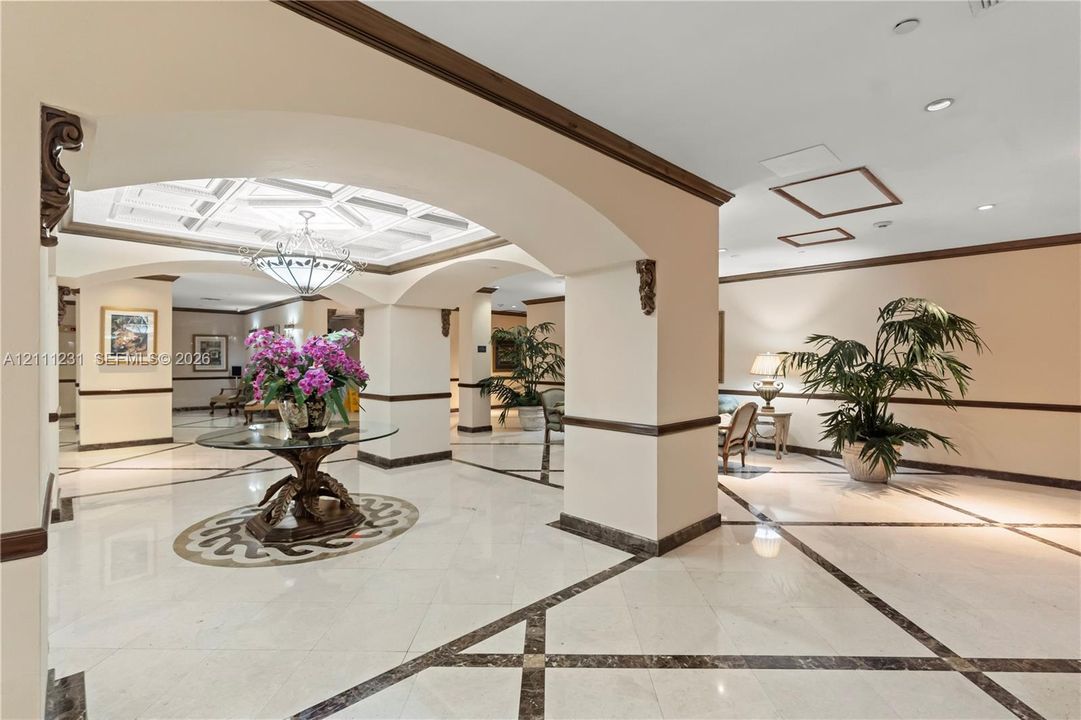 Grand foyer featuring large-format tile flooring with decorative stone inlays, coffered ceilings, structural arched openings, and custom millwork detailing