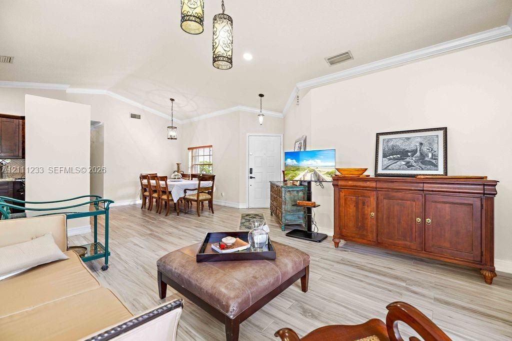 Open-concept interior featuring wood-finish flooring, vaulted ceilings with crown molding, and decorative pendant lighting