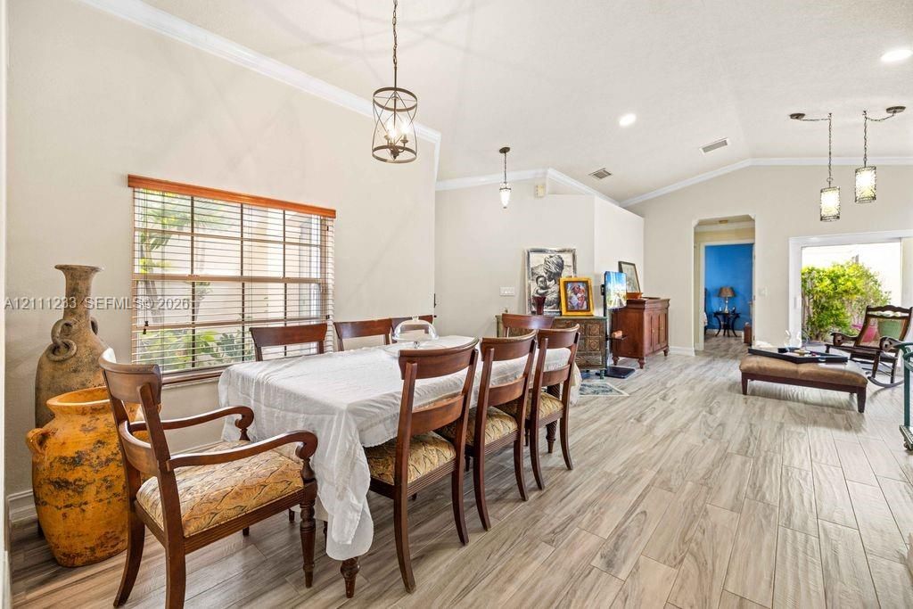 Open-concept dining area featuring vaulted ceilings, wood-finish tile flooring, crown molding, and multiple multi-light pendant fixtures