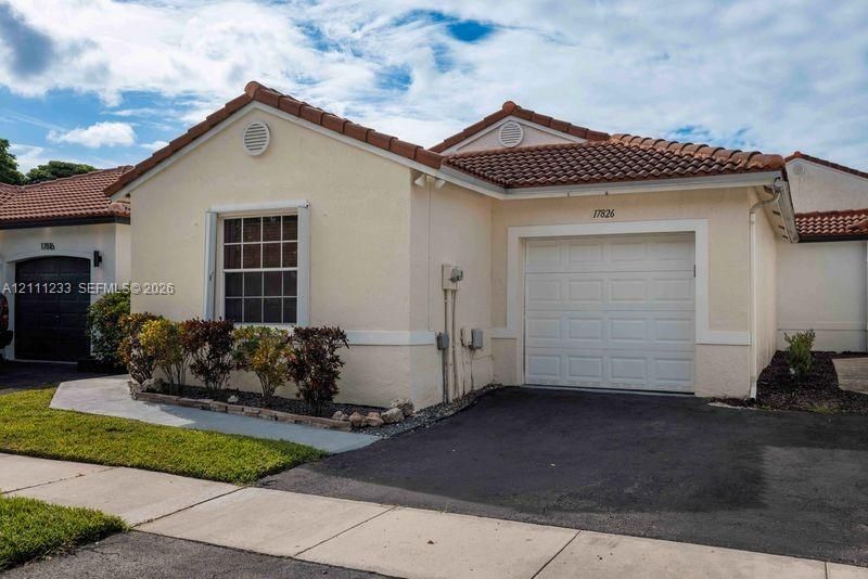 Stucco exterior featuring a terracotta tile roof, single-car garage, and established landscape beds