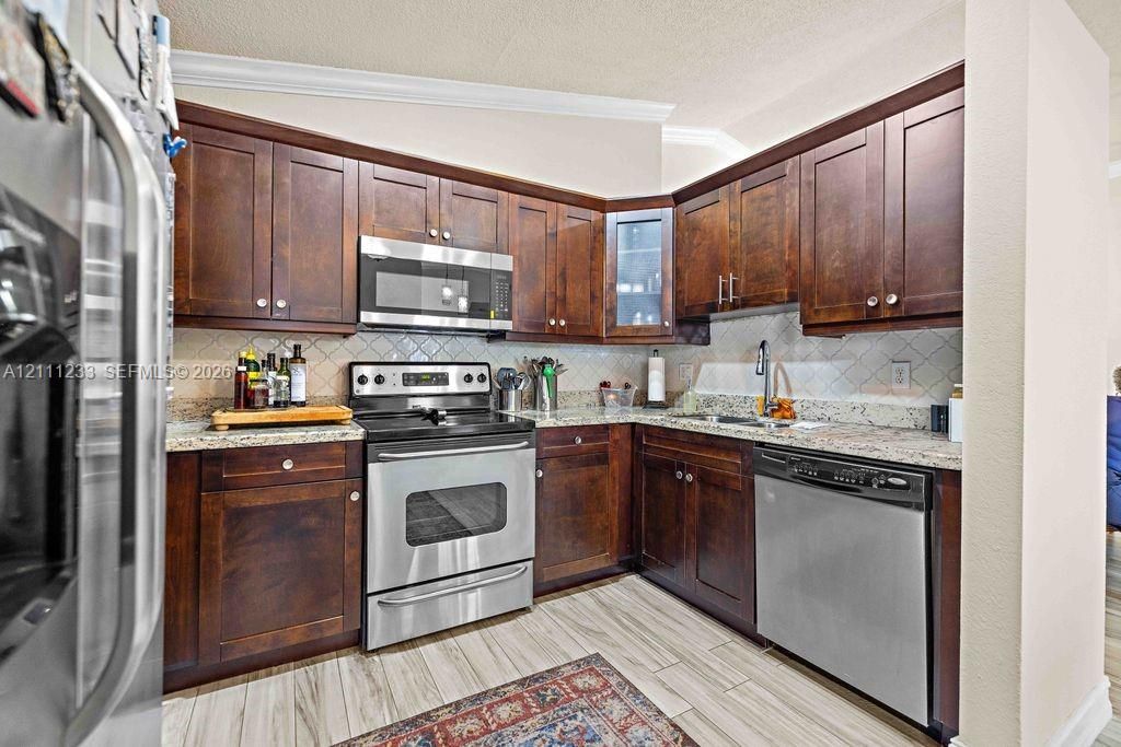 Kitchen featuring dark wood cabinetry, stone countertops, tiled backsplash, stainless steel appliances, and tile flooring