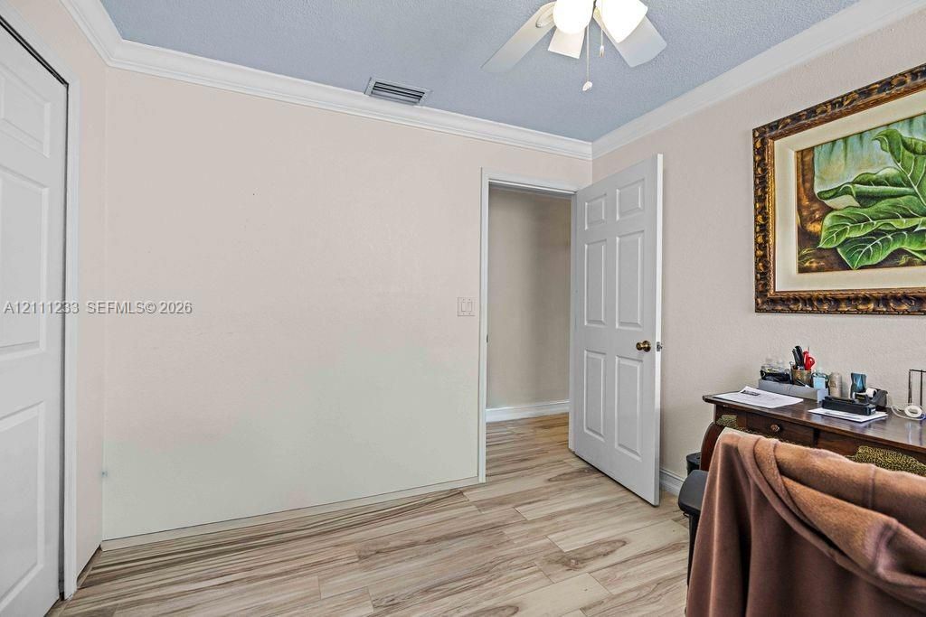 Room interior featuring wood-finish flooring, white six-panel interior doors, crown molding, and a ceiling fan with integrated light fixture