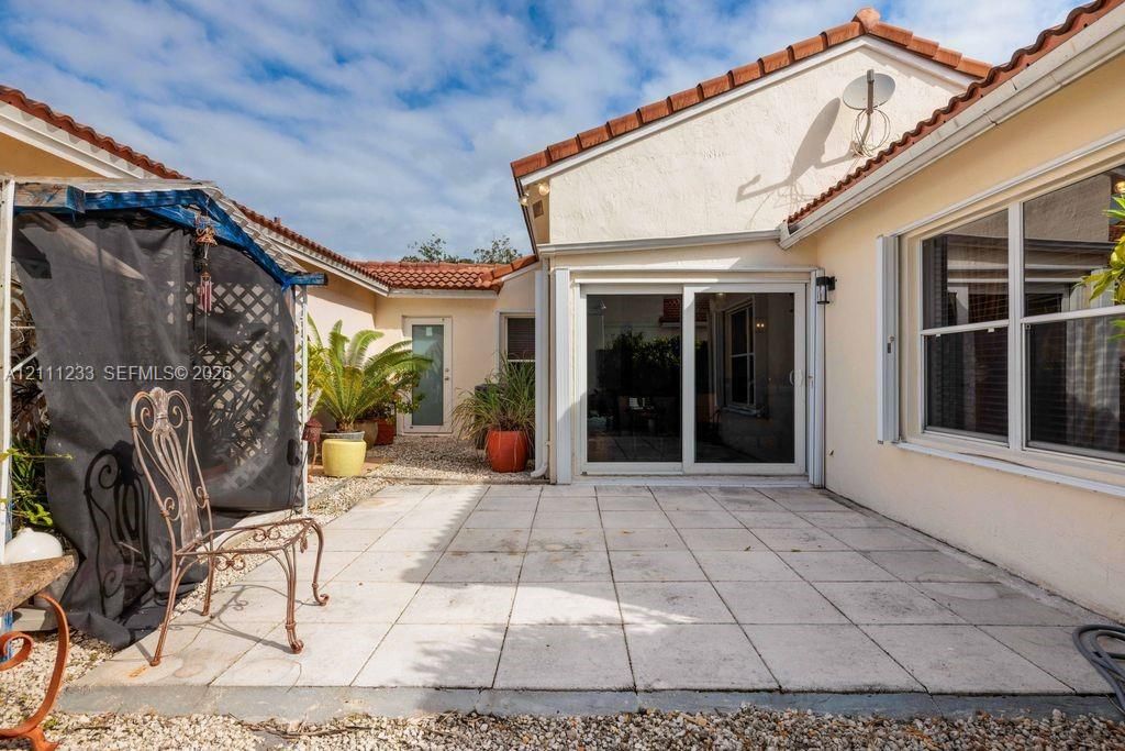 Stucco exterior courtyard featuring a paved tile patio, sliding glass door, and clay tile roof