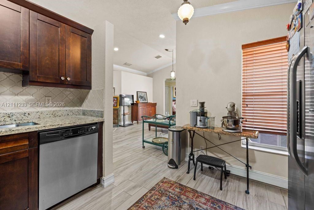 Kitchen featuring dark wood cabinetry, stone countertops, stainless steel dishwasher, arabesque tile backsplash, and wood-finish flooring