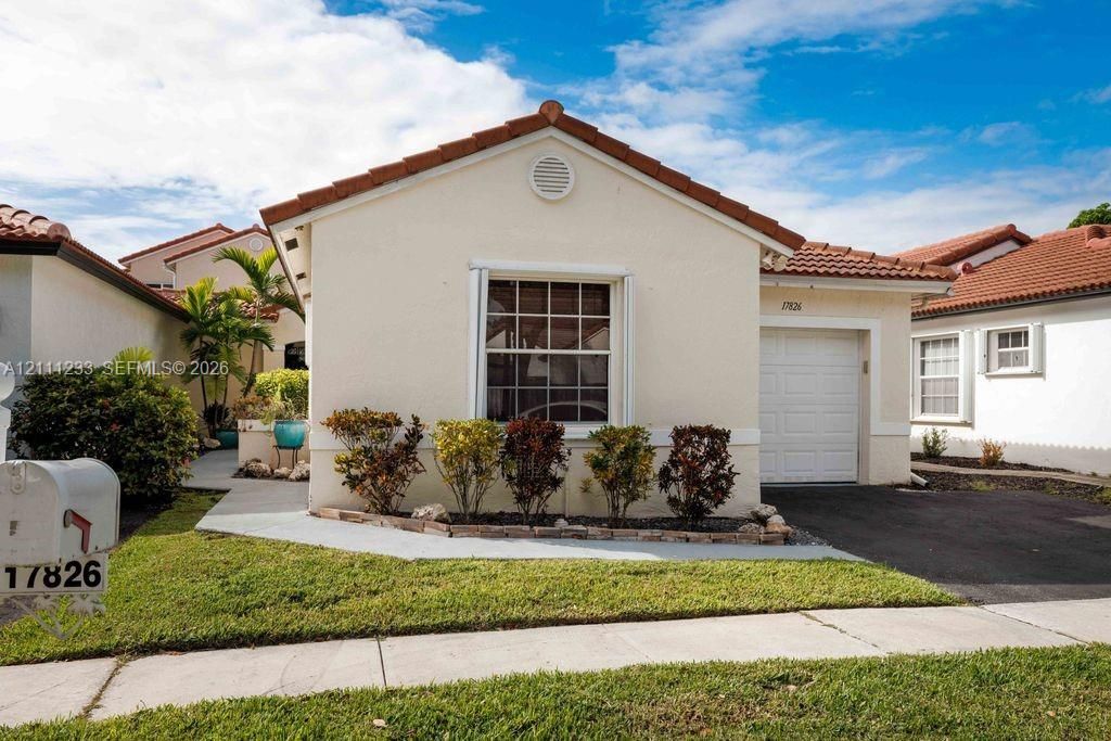 Stucco exterior featuring a terracotta tile roof, single-car garage, manicured landscape, and paved driveway