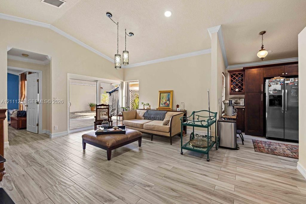 Vaulted ceilings with recessed lighting, wood-finish tile flooring, sliding glass doors, and dark wood cabinetry with built-in wine storage