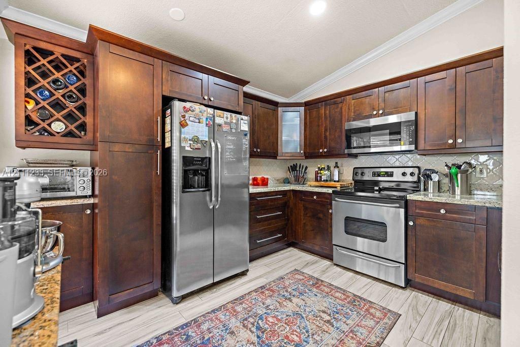 Kitchen featuring dark wood cabinetry, built-in wine rack, stone countertops, stainless steel appliances, and wood-finish tile flooring