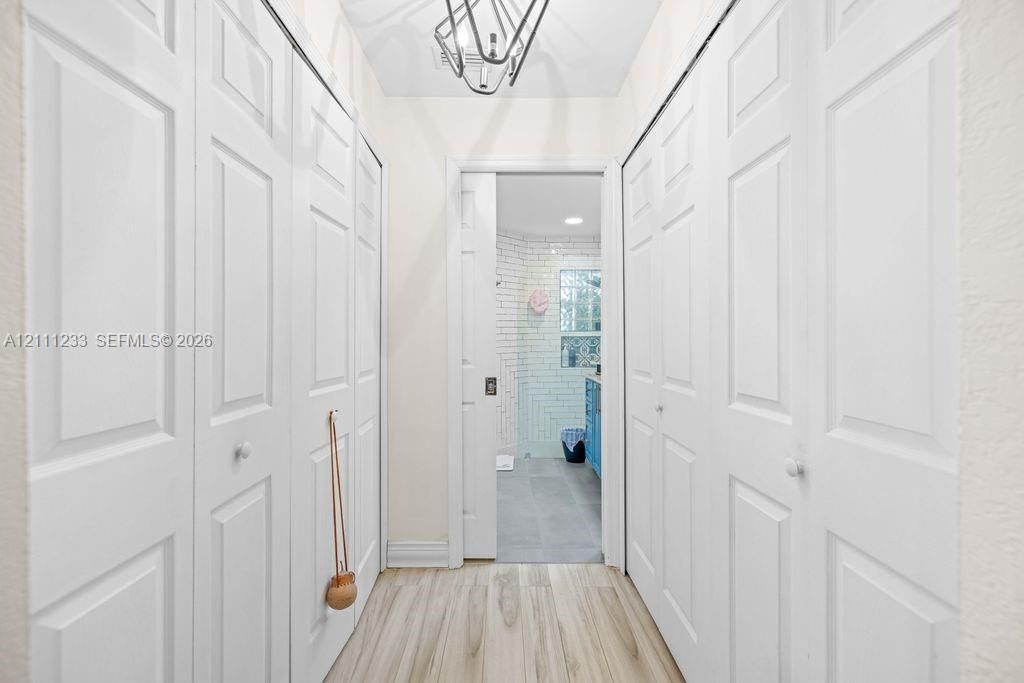Hallway featuring wood-finish flooring, dual sets of floor-to-ceiling bi-fold closet doors, and a geometric metal pendant light fixture
