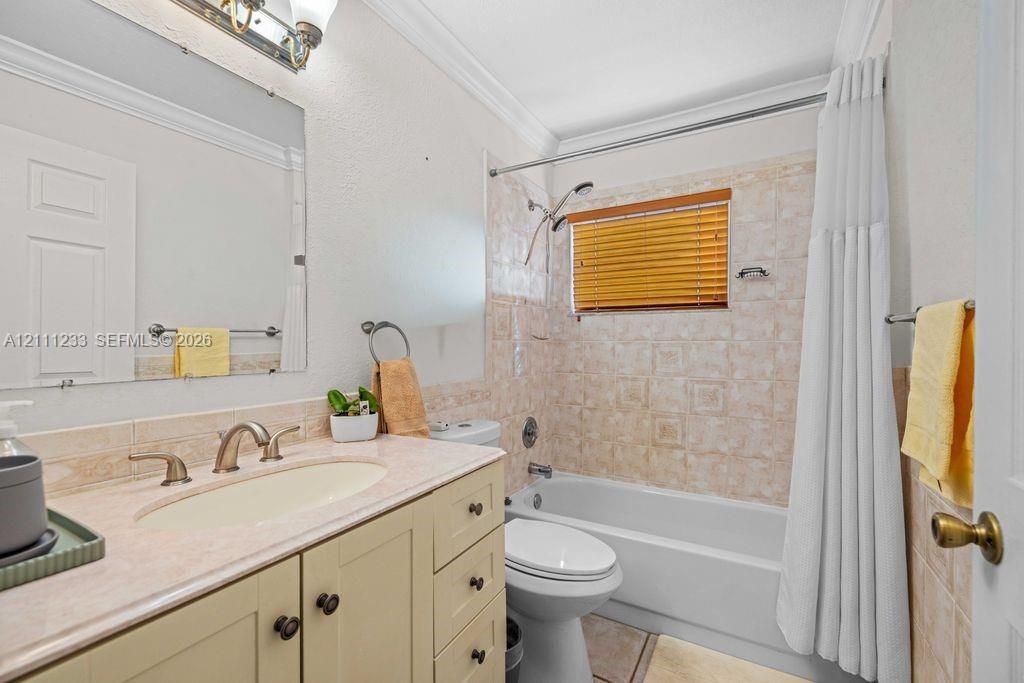 Bathroom featuring a vanity with a light-toned countertop, integrated basin, and brushed metal faucet, complemented by a combination tub and shower enclosure with patterned tile surround