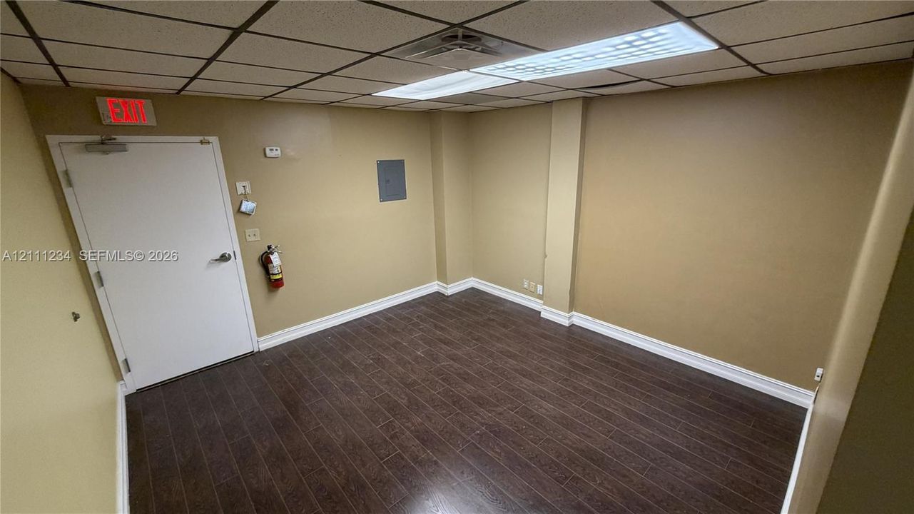 Interior space featuring dark wood-finish flooring, drop ceiling with recessed lighting, and a single-panel interior door
