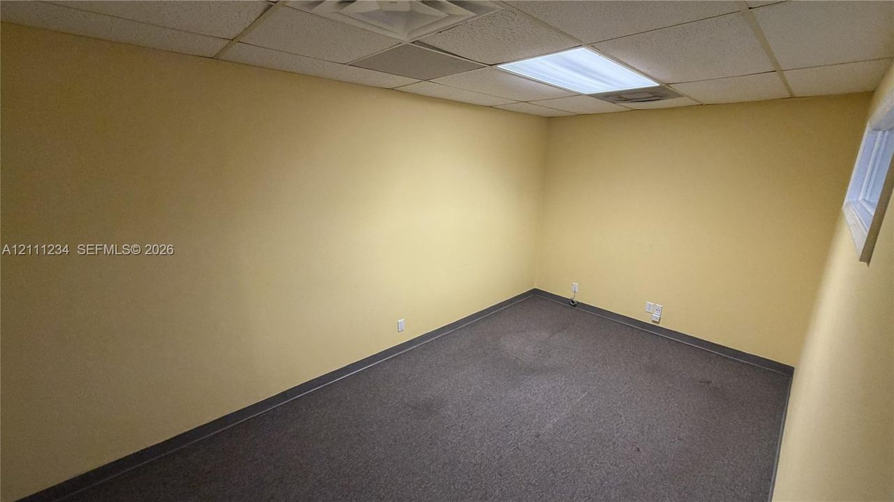 Interior room featuring wall-to-wall carpeting, a drop ceiling with integrated fluorescent lighting, and a window